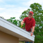 Wind mitigation inspection inspector on a ladder doing inspection on new roof to create a report and risk rating for homeowner to send to their insurance company to receive deductions in policy costs.